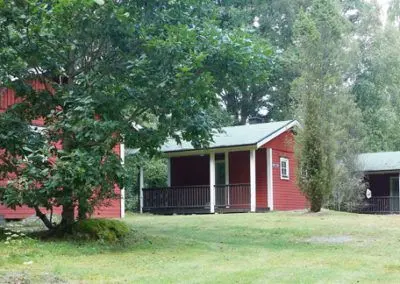 Röd stuga med veranda under stora lövträd